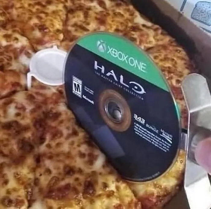 Xbox One Halo game disc being used to cut a cheese pizza in a topsy-turvy, nonsensical visual.