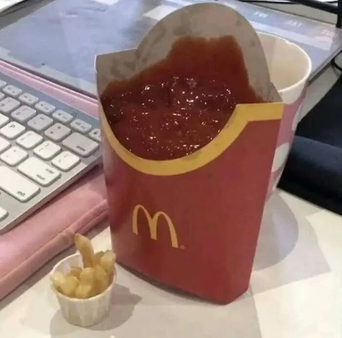 A large McDonald's fries container filled with ketchup next to a tiny cup holding a few fries, making no sense.