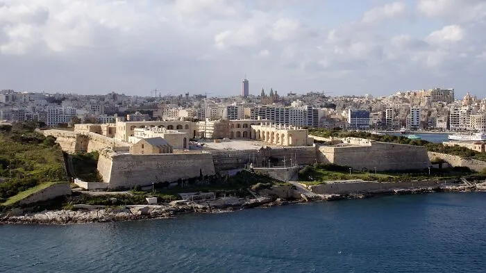 Historic building near water with stone fortifications and cityscape in the background, representing saved historic architecture.