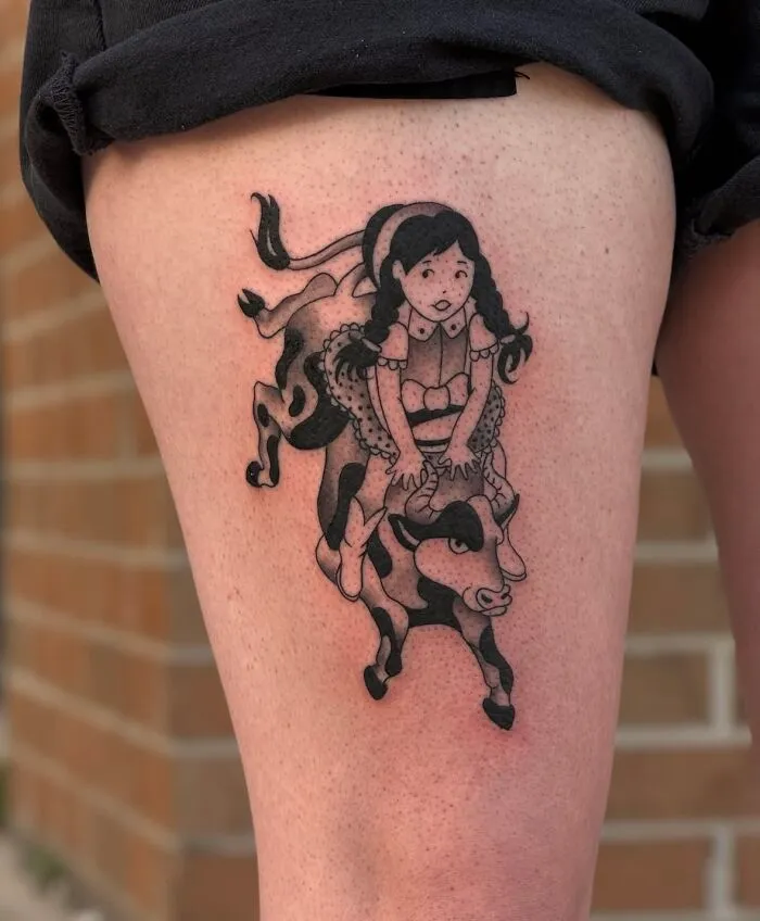 Black and gray tattoo of a girl riding a spotted bull on the thigh, showcasing one of the best tattoos popular on social media.