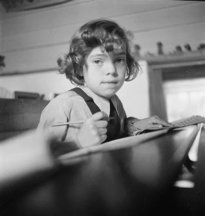 Young student in a classroom writing with pencil, vintage black and white photo of schools worldwide during World War II.