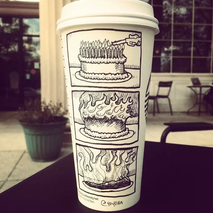 Coffee cup with a humorous cartoon showing a cake set on fire in three comic panels outside a cafe.