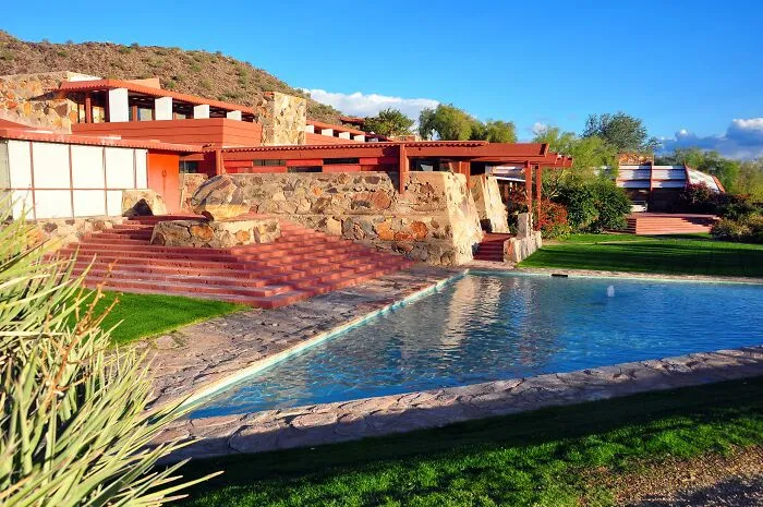 Historic homes with stone walls and red terraces featuring a reflecting pool under a clear blue sky in America’s architectural heritage.