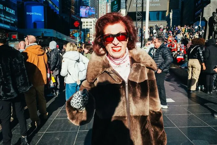 Woman in a fur coat and sunglasses smiling among a busy crowd in New York City street captured in powerful street moments.