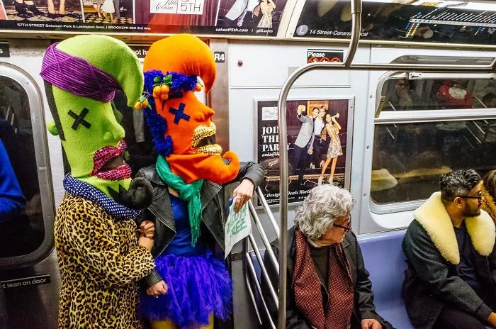 Two passengers in colorful, oversized masks and costumes capture powerful street moments on a New York City subway train.