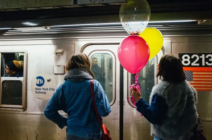 Two women with colorful balloons stand on a New York City subway platform in a powerful street moment of NYC.