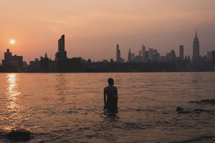 Person standing in water at sunset with NYC skyline in the background, capturing powerful street moments in NYC.