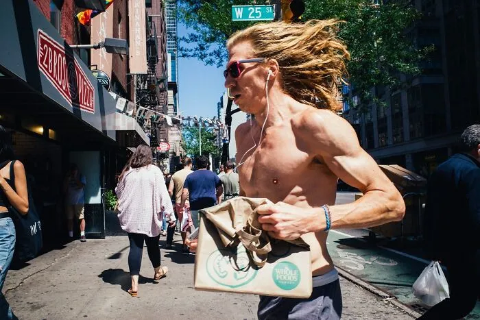 Shirtless man with long hair running on a busy NYC street, captured in a powerful street moment in NYC.