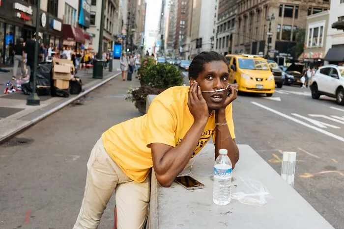 Man wearing oxygen tube and yellow shirt leaning on a street barrier, captured in powerful NYC street moments photography.