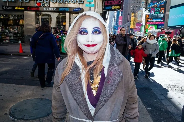 Woman with white face paint and colorful eye makeup smiling on busy NYC street, street moments captured by photographer.