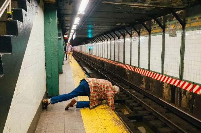 Man in plaid jacket leaning over edge of subway platform capturing powerful street moments in NYC underground station.