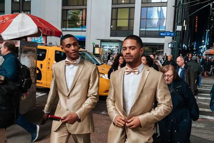 Two men in gold suits walking on a busy NYC street, capturing powerful street moments in New York City nightlife.