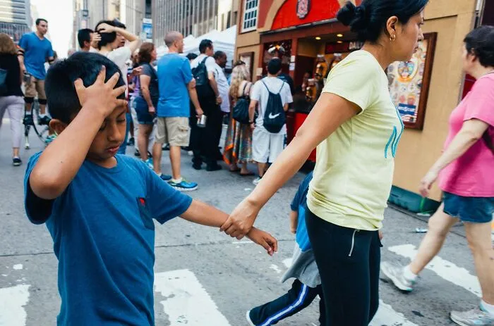 Crowded NYC street scene with a woman holding a child's hand, capturing powerful street moments in urban life.