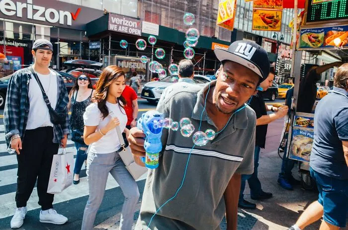 Man blowing bubbles on busy NYC street with pedestrians in background, capturing powerful street moments of NYC.