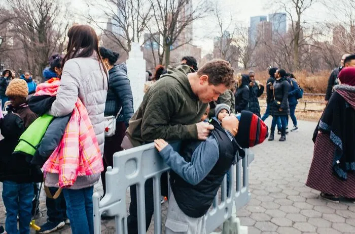 A candid moment in NYC streets showing diverse people interacting near a park on a cold day in the city.