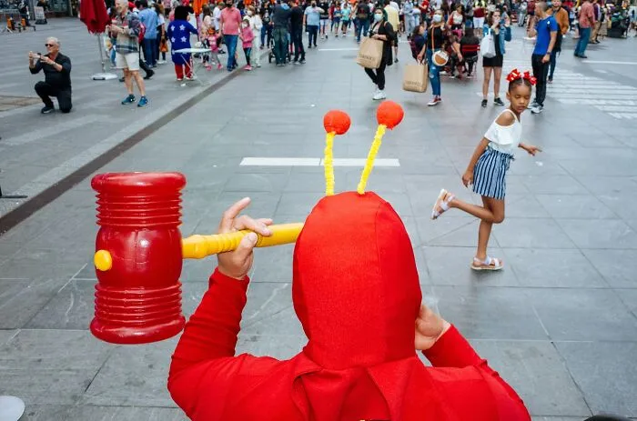 Street performer in red costume with giant hammer entertaining onlookers in busy NYC street capturing powerful street moments.