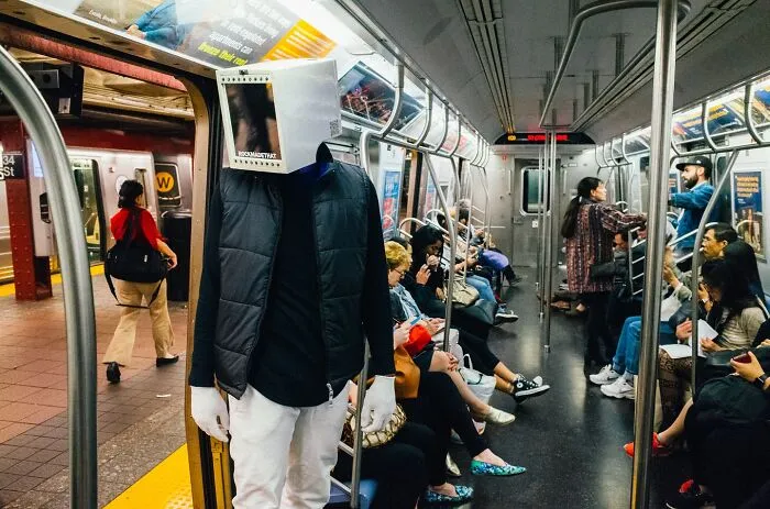 Man wearing a unique covered face mask stands inside a busy NYC subway car capturing street moments.