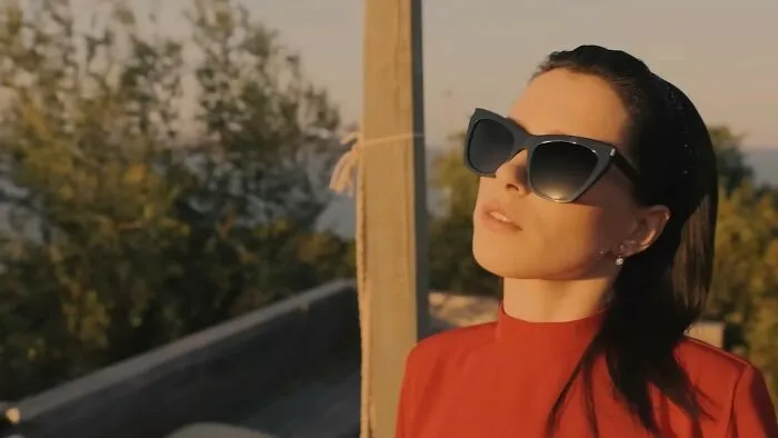 Woman wearing large black sunglasses and red top, looking outdoors with a thoughtful expression related to worst movies.