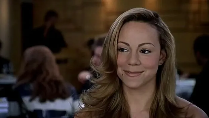 Actress Mariah Carey in a scene from one of the worst movies of all time, showing a subtle smile in a dimly lit setting.