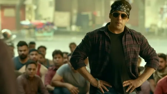 Man wearing sunglasses and a bandana stands confidently in front of a crowd in a scene from worst movies of all time.