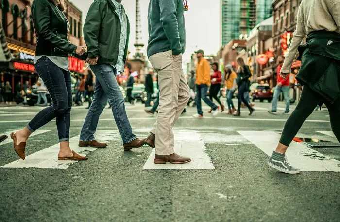 People walking across a busy city street in the U.S. with vibrant urban buildings in the background.