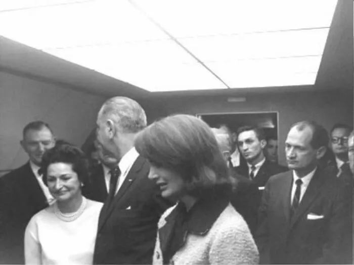 A black and white historic photo of several people indoors with a tense atmosphere, linked to terrifying and horrific backstories.
