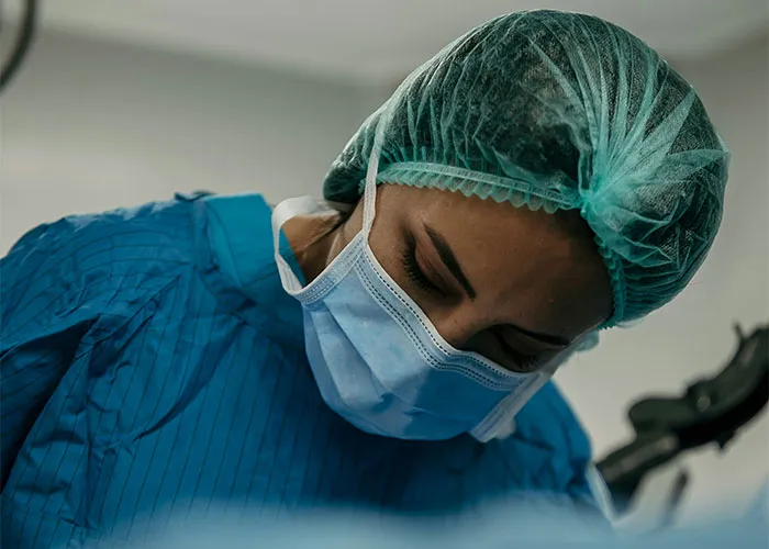 Médico con mascarilla y gorro quirúrgico en sala de operaciones atendiendo casos médicos urgentes y complejos.