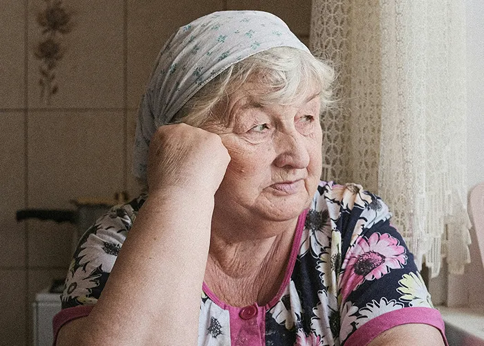 Elderly woman wearing a headscarf, looking thoughtfully out the window, symbolizing concerns about death machines.
