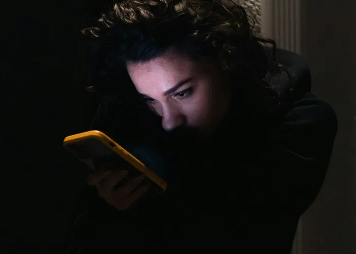 Person with curly hair looking intently at a phone screen in a dark room, illustrating concerns about death machines.