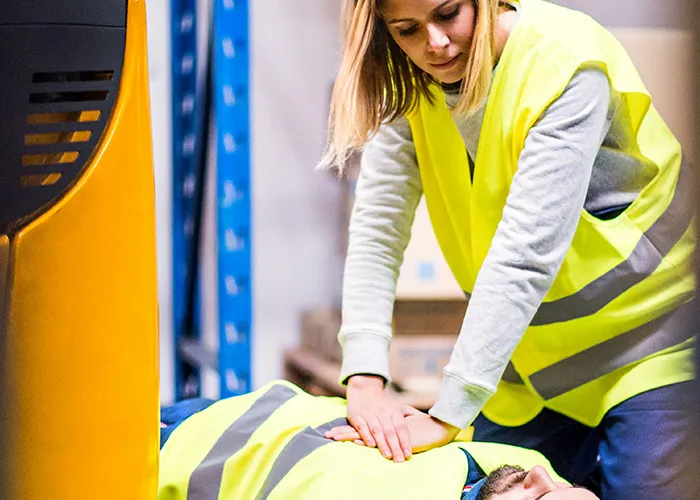 Woman performing CPR on a man in safety vests, highlighting doctors' warnings about death machines in the workplace.