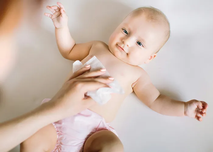Baby lying down while an adult cleans their chest with a wipe, highlighting doctors' insights on health and care.