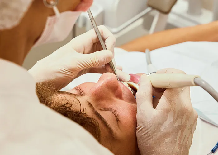 Dentist wearing gloves performing a dental cleaning on a male patient at a modern dental clinic.