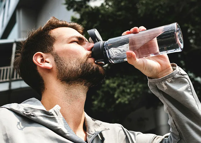 Man drinking water from a bottle outdoors, illustrating health awareness and doctors' advice on death machines risks.