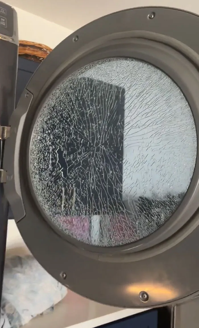Cracked glass door of a washing machine showing a funny unfortunate situation of forgotten item damage.