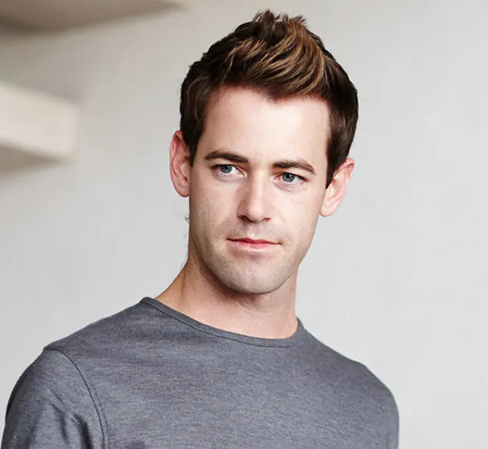 Young single man with styled hair wearing a gray shirt, reflecting on behaviors that affect romance prospects.