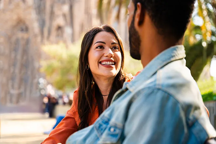 A smiling woman and a man in a denim jacket engaged in conversation, highlighting single male behaviors affecting romance.