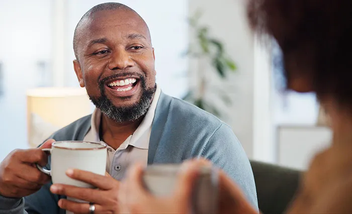 Man displaying single male behaviors while enjoying a warm drink and conversation with a woman indoors.