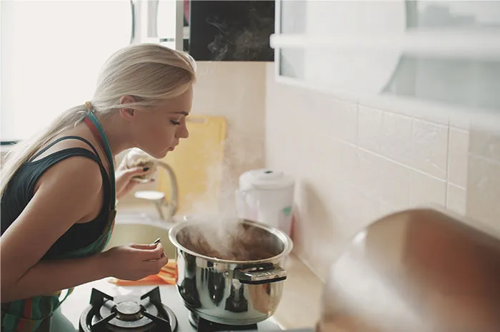 Woman in kitchen leaning over steaming pot, uncovering cooking secrets and ingredients they don’t usually reveal.