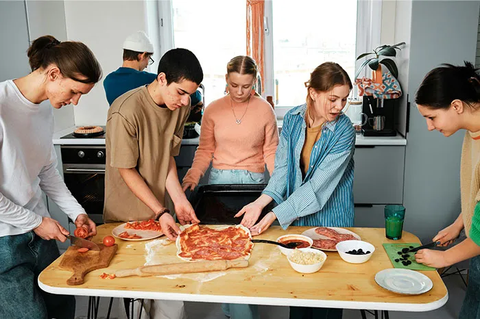 A group of young people preparing pizza together, sharing cooking secrets and unique ingredients in a bright kitchen.