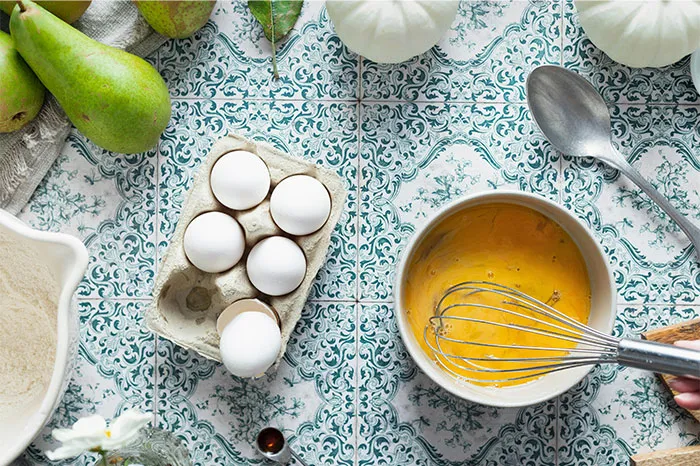 Whisking eggs in a bowl with fresh ingredients on patterned surface, sharing cooking secrets and hidden ingredients.