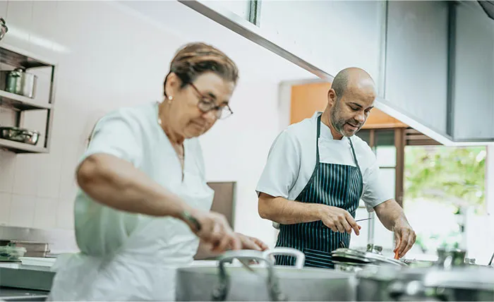 Two chefs in a professional kitchen sharing cooking secrets and unique ingredients while preparing food together.