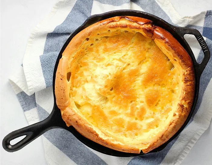 Dutch baby pancake cooked in a cast iron skillet, showcasing a golden crust with cooking secrets and ingredients revealed.