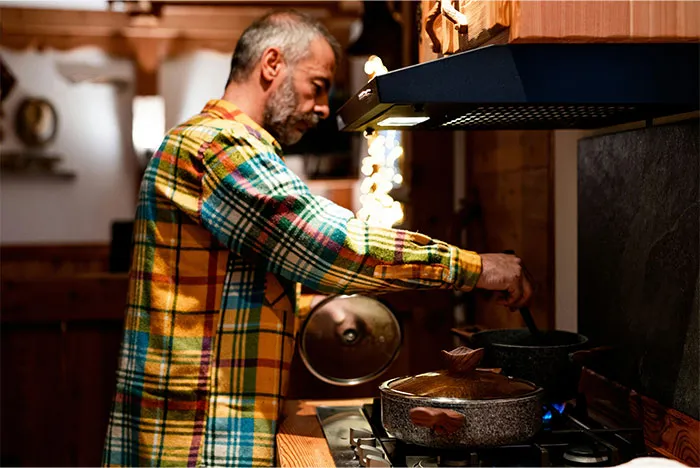 Man cooking in a warm kitchen, sharing cooking secrets and ingredients they don't usually reveal while stirring a pot on the stove.