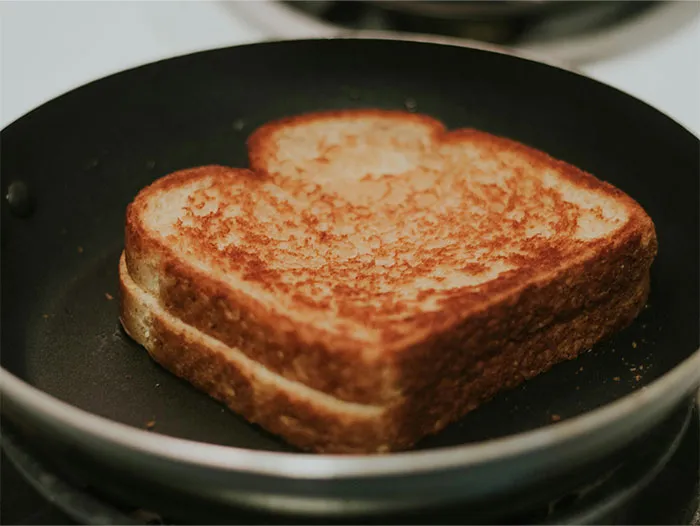 Golden grilled sandwich cooking in a black pan revealing simple cooking secrets and ingredients for a perfect toast.