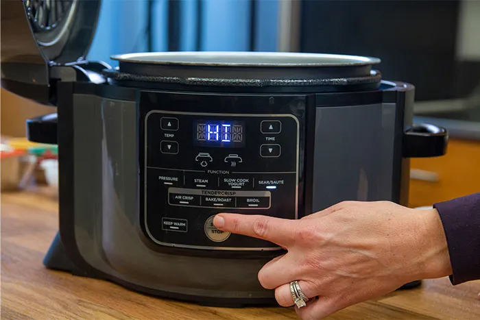 Hand pressing start button on electric pressure cooker, highlighting cooking secrets and useful kitchen ingredients.