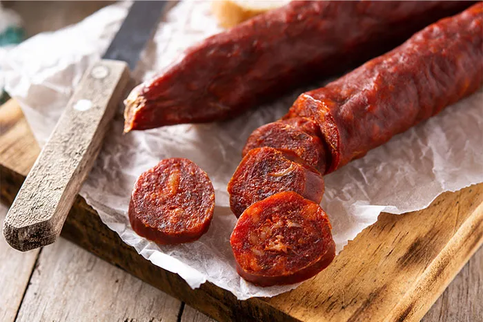 Close-up of sliced spicy sausage on parchment paper with a knife, highlighting cooking secrets and ingredients.