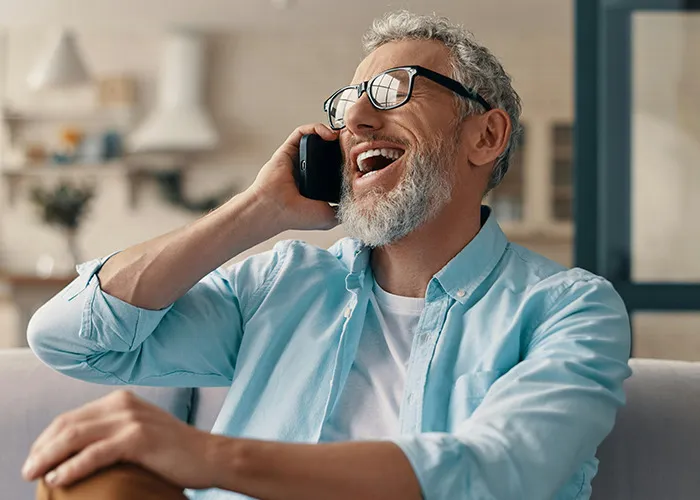 Older man with gray hair and glasses laughing while talking on a phone, representing savage insults conversation.