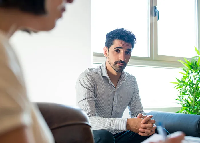 Man with serious expression listening to a woman in a bright room, illustrating savage insults and tense conversations.