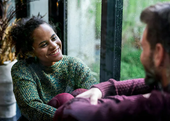 Two people having a friendly conversation indoors by a window, illustrating social interaction and communication skills.
