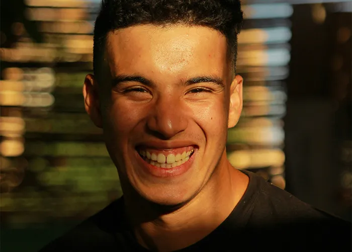 Young man smiling brightly in natural light, capturing a moment of joy and confidence in a casual setting for savage insults content.